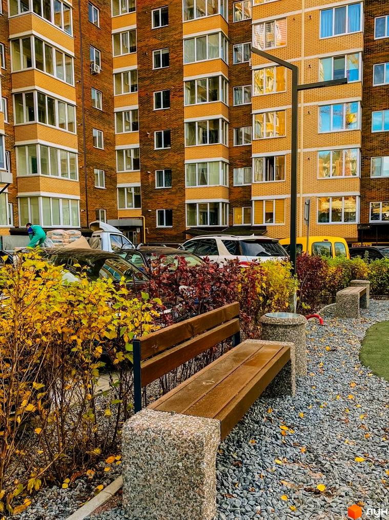 Житловий комплекс Преміум Парк: цегляний будинок з жовтими вставками та балконами. Прибудинкова територія з лавками, кущами та гравієм.