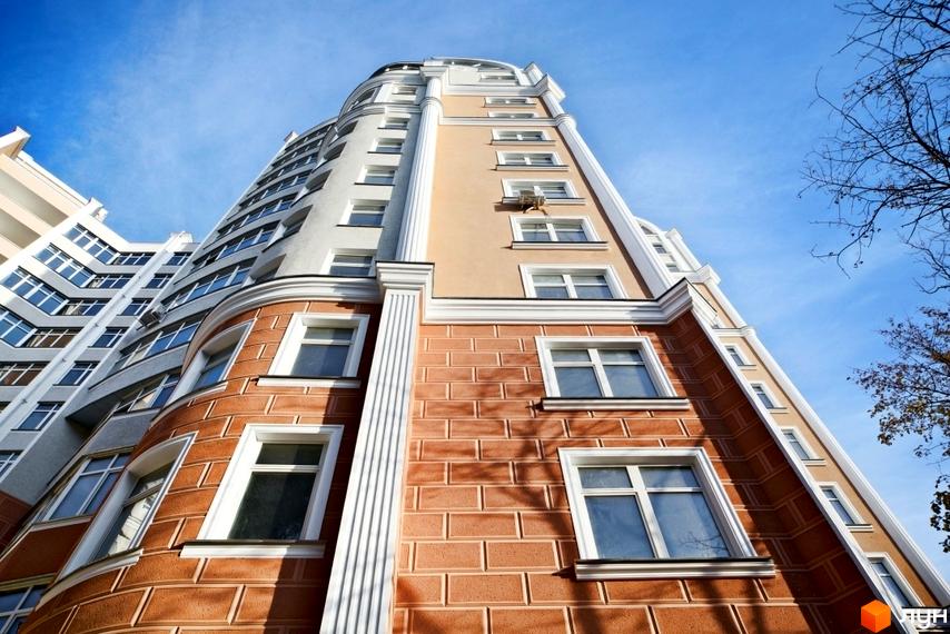 Житловий комплекс по провулку Каркашадзе, 9. Висотна будівля з цегляним фасадом та великими вікнами на тлі блакитного неба.