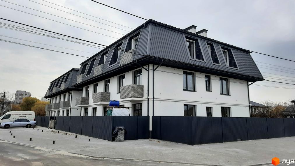 Зовнішній вигляд новобудови на вулиці Вчительська, 16, з сірим дахом та білими стінами, огороджена темним парканом. На прибудинковій території видно автомобіль та пішохідну зону.