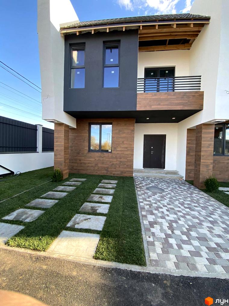 Таунхауси Royal life. Фасад будинку з темними та дерев'яними елементами, великими вікнами та балконом. Прибудинкова територія з доріжкою з плитки та зеленою галявиною.