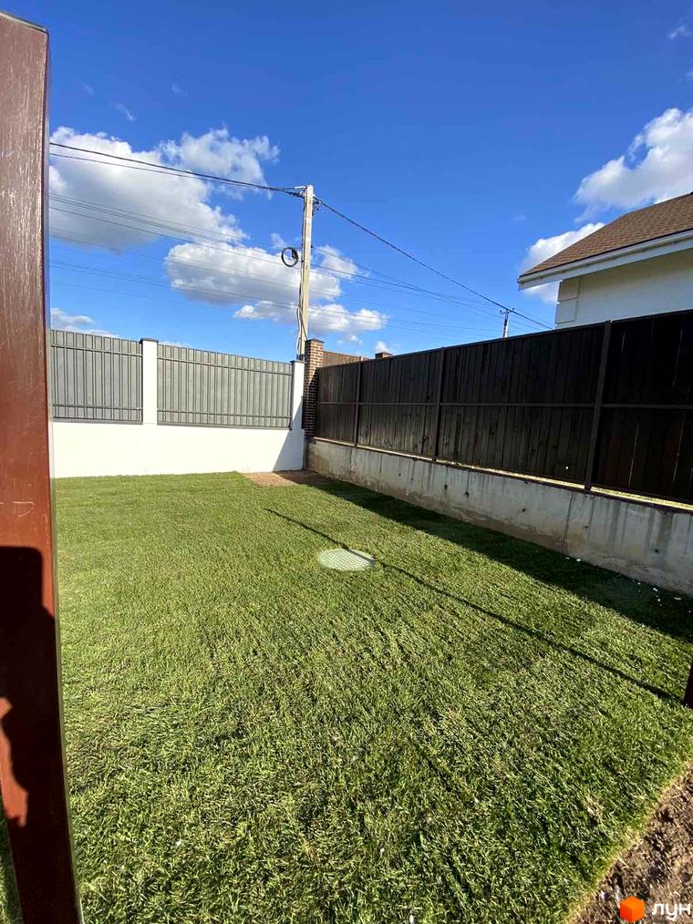 Таунхауси Royal life: зелений газон та паркан. Зелена ділянка перед будинком з парканом та блакитним небом.