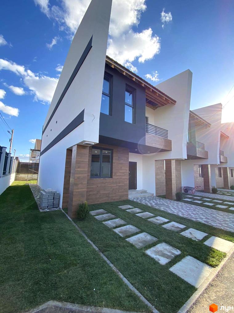 Таунхауси Royal life з білими та темними фасадами, дерев'яними елементами та балконами. Перед будинками зелений газон з квадратними плитками та бруківкою.