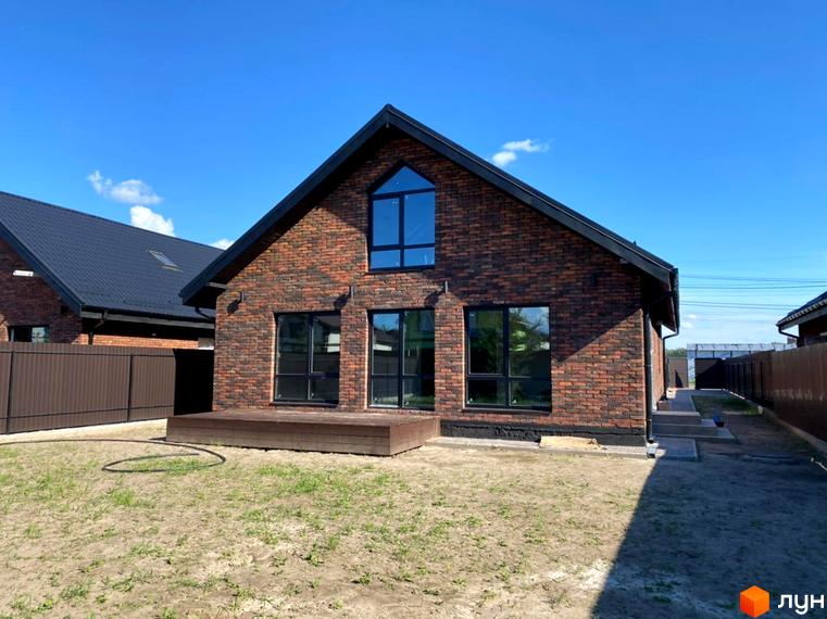 Котеджне містечко КМ Одноповерховий Київ - Гореничі. Будинок з червоної цегли з великими вікнами та терасою на тлі блакитного неба.