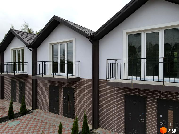 Триповерховий будинок з балконами та цегляною кладкою на фасаді. На прибудинковій території викладена плитка, висаджені невеликі дерева.