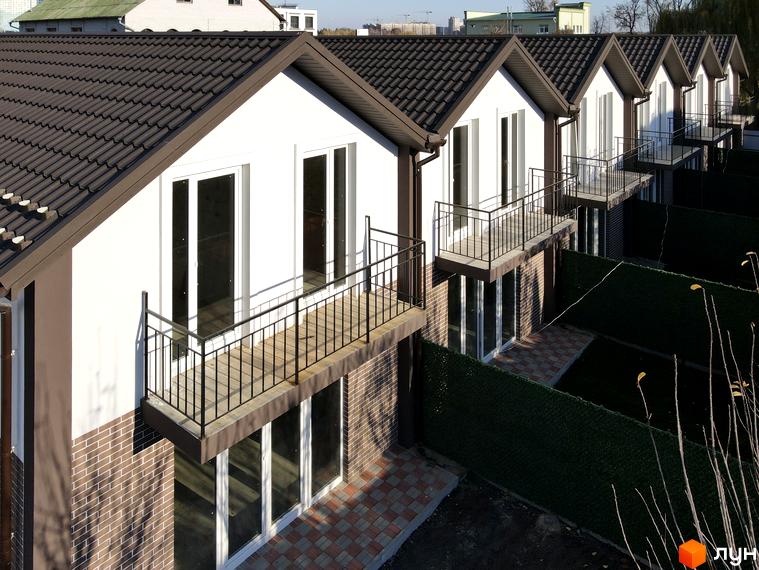 Зображення сторінки ЖК Таунхаус на Інститутській. Ряд будинків з балконами та коричневою черепицею на даху. На прибудинковій території зелений газон та плитка.