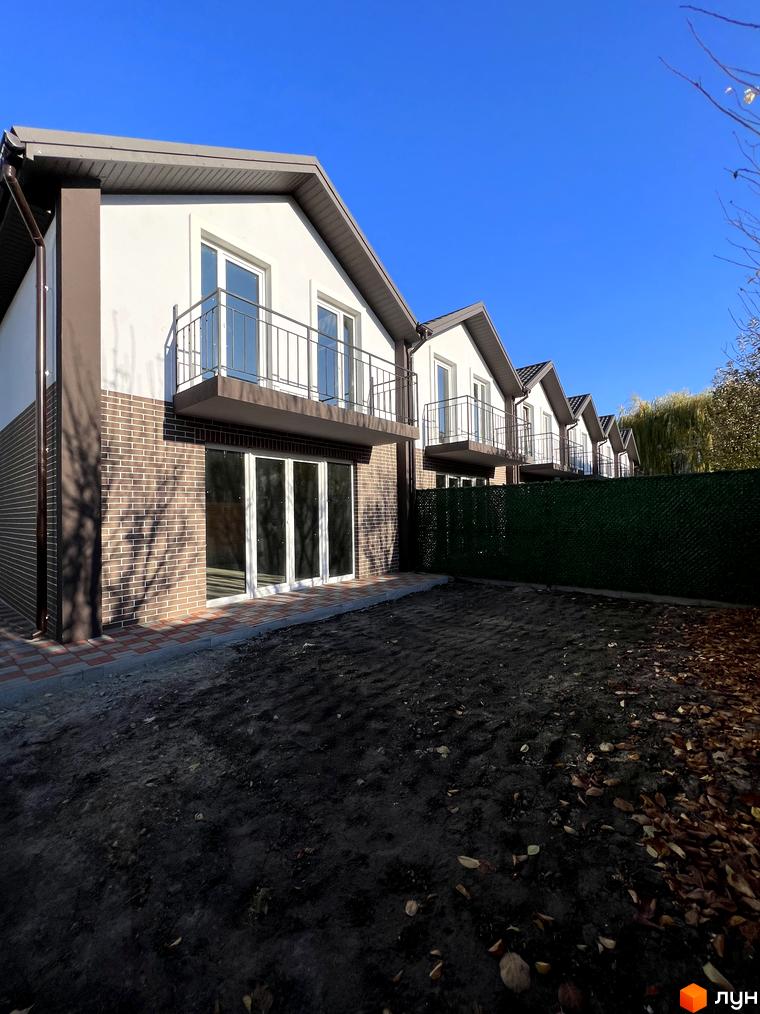 Зображення житлового комплексу. Будинки з білими стінами та коричневою цегляною кладкою, балконами та великими вікнами. На передньому плані - територія з землею.