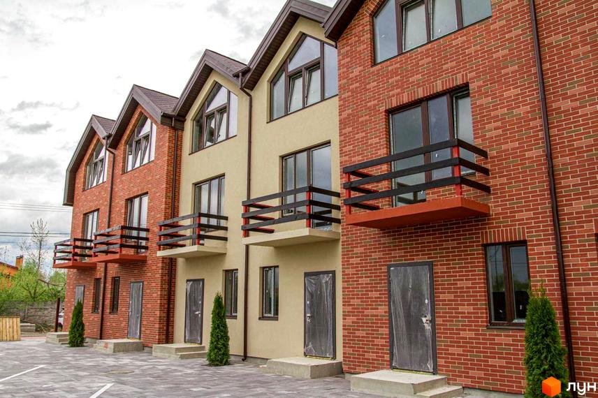 Зовнішній вигляд таунхаусів Modern House з балконами. Будинки з червоної цегли та бежевого кольору, перед будинками висаджені туї.