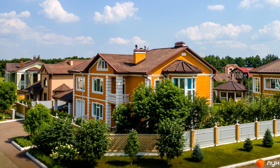 Котеджне містечко КМ Home Resort: двоповерхові будинки з жовтими фасадами, коричневими дахами та зеленими деревами. Огороджена територія з парканом та газоном.