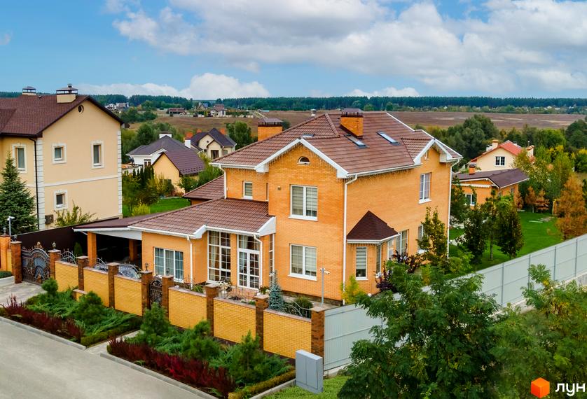 Котеджне містечко КМ Home Resort: двоповерховий цегляний будинок з коричневим дахом, огороджена територія з зеленими насадженнями та парканом.