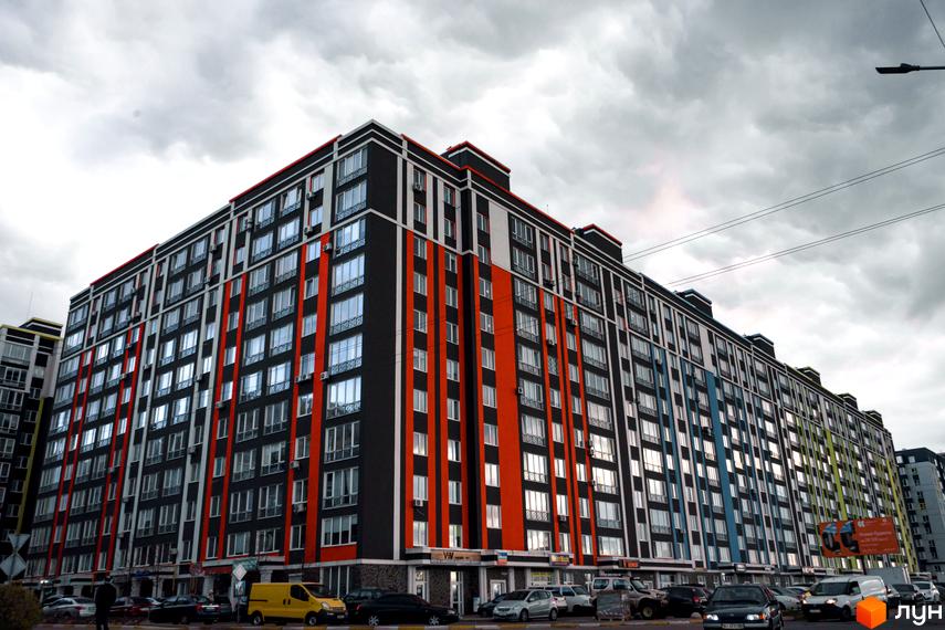 Багатоповерхова новобудова ЖК Фортуна-2 з фасадом у чорному, білому та помаранчевому кольорах. На першому поверсі розташовані комерційні приміщення, перед будинком припарковані автомобілі.