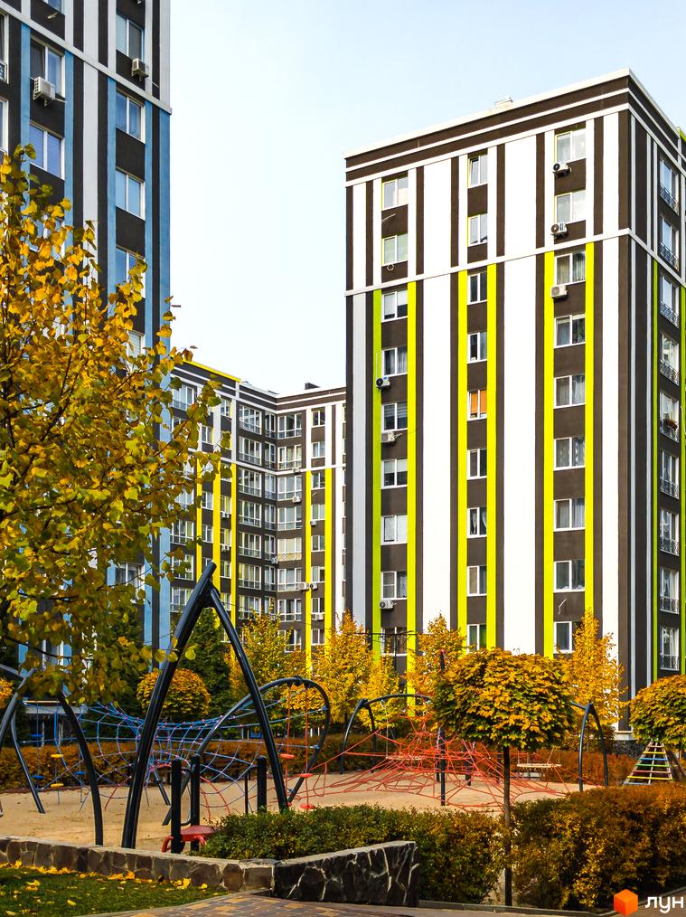 Житловий комплекс Фортуна-2 з фасадами в смужку та дитячим майданчиком. На території комплексу є дерева з жовтим листям.