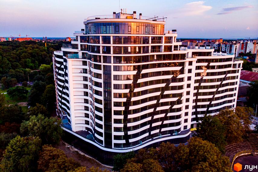 Зображення Житлового комплексу Parus. Багатоповерхова будівля з хвилястими білими балконами та панорамними вікнами, оточена зеленню дерев.