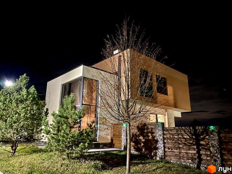 Зображення фасаду будинку в Котеджному комплексі Crystal Forest вночі. На передньому плані видно дерева та огорожу з декоративним освітленням.