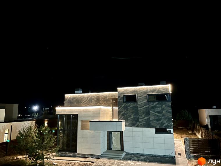 Зображення будинку у новому житловому районі Crystal Forest вночі. На фасаді будинку світлодіодне підсвічування, навколо будинку є дерева та огорожа.