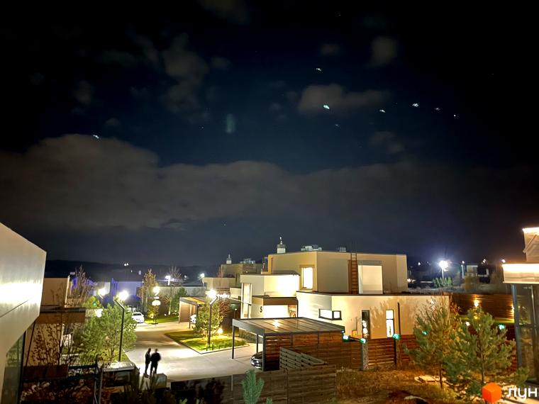 Зображення житлового комплексу КМ Crystal Forest вночі. На фото видно будинки з підсвічуванням, а також прибудинкову територію з деревами та ліхтарями.