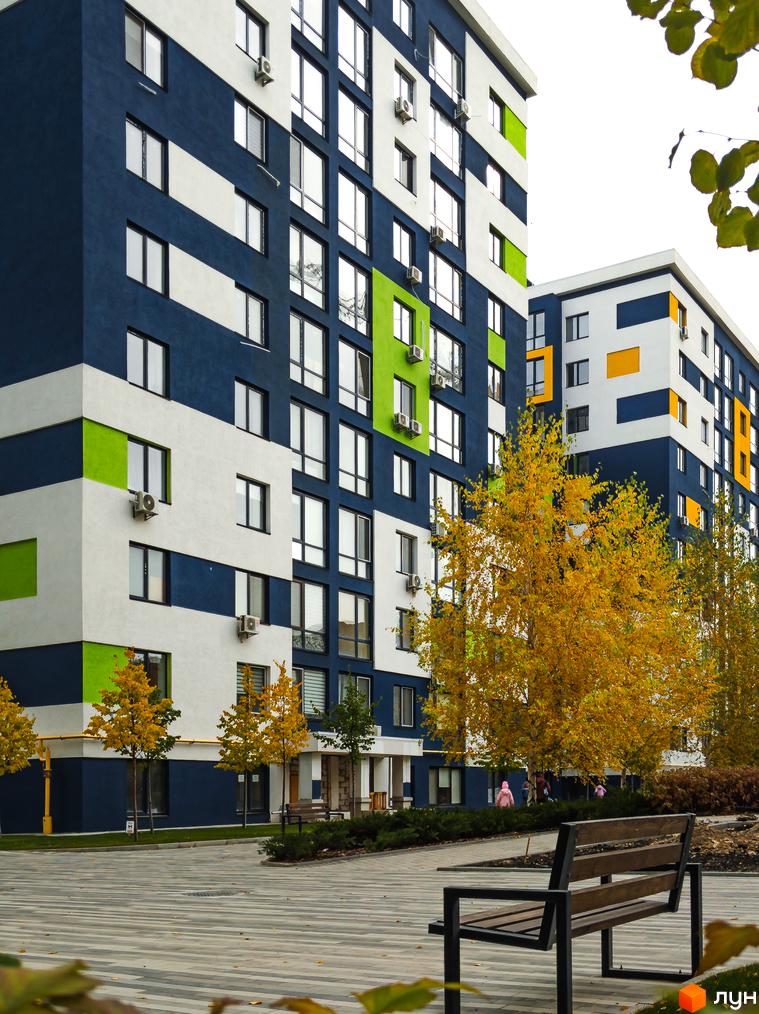 Житловий комплекс Модуль з яскравим фасадом та зеленими зонами. Сучасна архітектура новобудови та облаштована прибудинкова територія з деревами та лавками.
