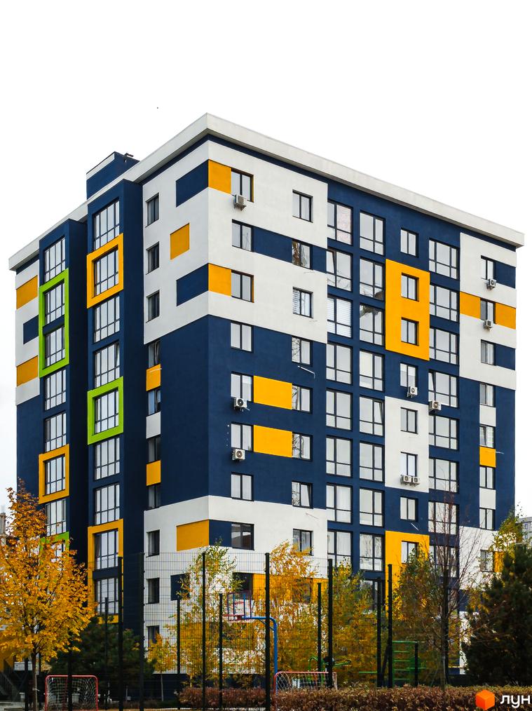Багатоповерховий будинок Житлового комплексу Модуль з фасадом синього, білого та жовтого кольорів. На передньому плані осінні дерева та спортивний майданчик.