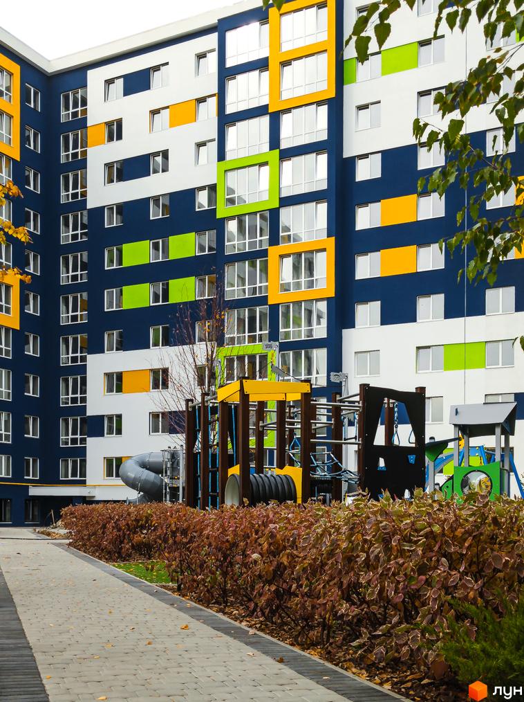 Житловий комплекс Модуль з темно-синім фасадом, білими, жовтими та зеленими вставками. На прибудинковій території дитячий майданчик та доріжка.