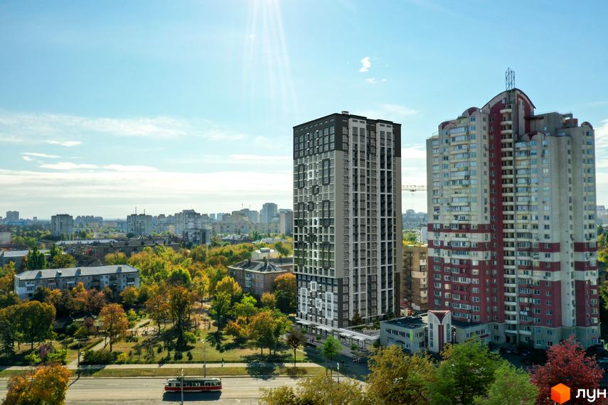 Новобудова ЖК Квітень з сірими та чорними фасадами на фоні міського пейзажу та парку з осінніми деревами. Поруч розташована багатоповерхова будівля з червоними елементами.