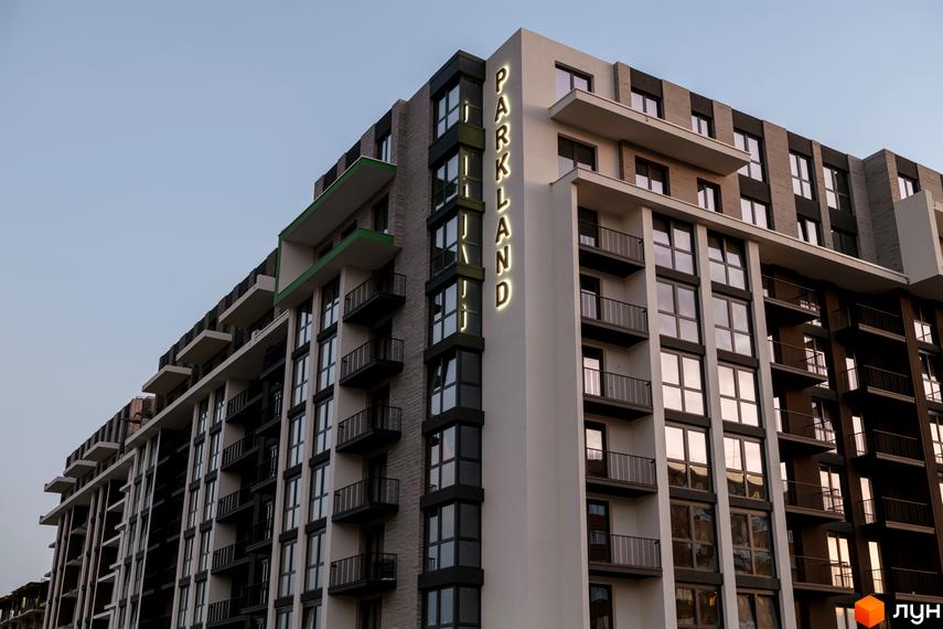 Зовнішній вигляд новобудови PARK LAND: багатоповерховий будинок з балконами та підсвіченою вивіскою на фасаді.