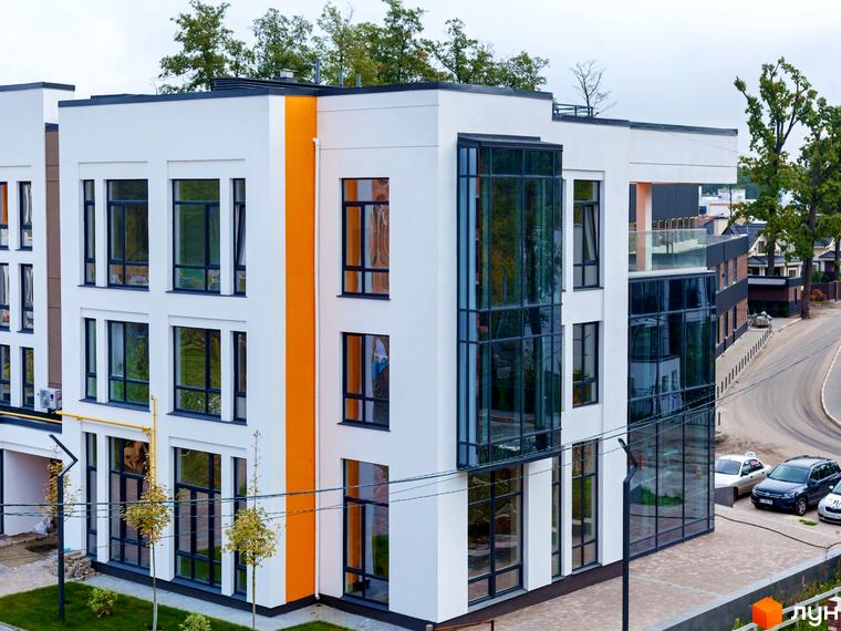 Білий будинок Житлового комплексу Найкращий квартал з великими вікнами та помаранчевою вертикальною смугою на фасаді. Поруч зелені насадження, вимощена територія та дорога.