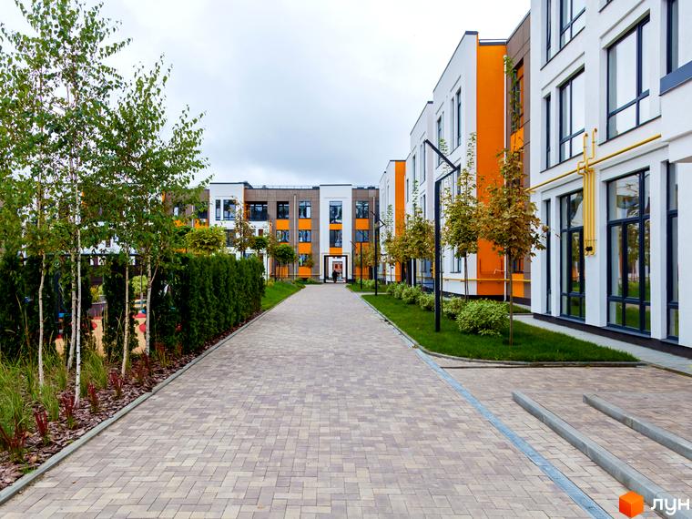 Вигляд фасаду та пішохідної зони Житлового комплексу Найкращий квартал. Багатоповерхові будинки з великими вікнами, доглянута територія з деревами та газонами.
