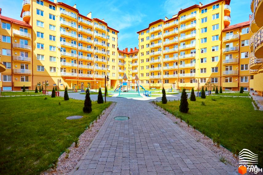 Житловий комплекс САКУРА: жовті багатоповерхові будинки з балконами, внутрішній двір з дитячим майданчиком та зеленими насадженнями.