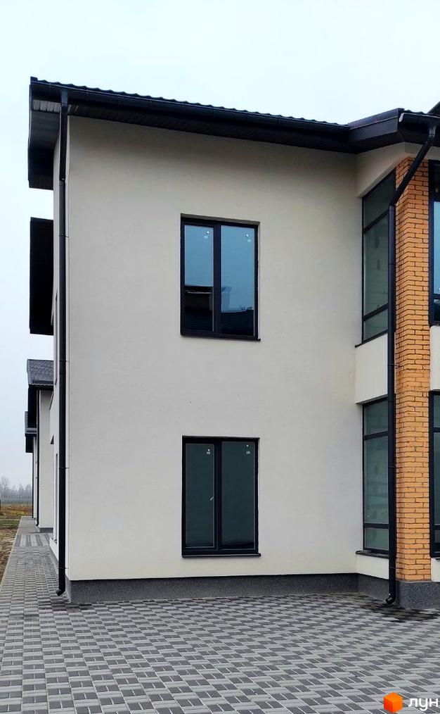 Зовнішній вигляд будинку ЖК Лелека з білою штукатуркою та цегляним оздобленням. Поруч розташована вимощена сірими плитками прибудинкова територія.