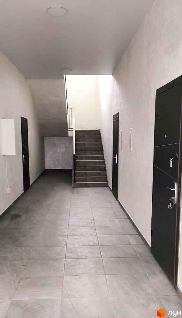 Парадний вхід до житлового комплексу Лелека з дверима та сходами. Відкритий простір та сіра плитка на підлозі.