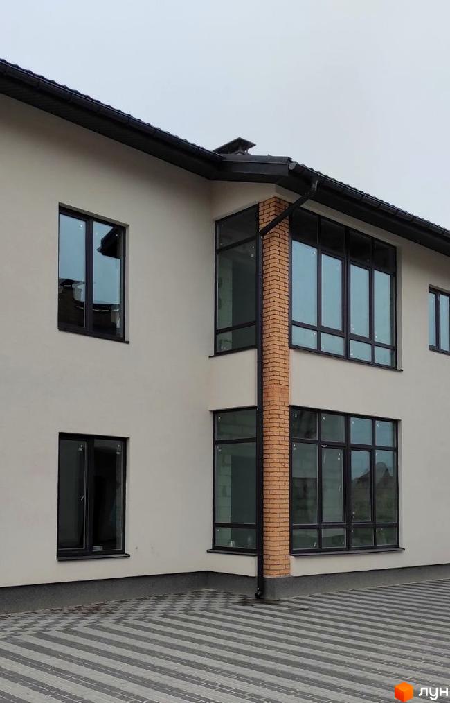 Зовнішній вигляд новобудови ЖК Лелека з великими вікнами та цегляною колоною. Навколо будинку розташована прибудинкова територія з візерунчастим покриттям.