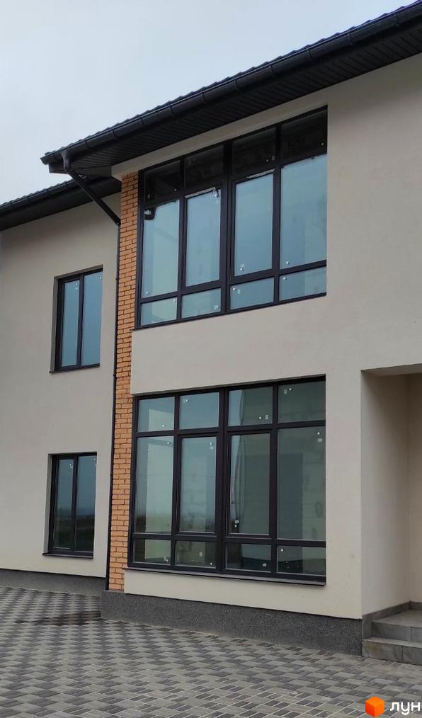 Двоповерховий будинок ЖК Лелека з великими вікнами та цегляною вставкою. На подвір'ї бруківка.