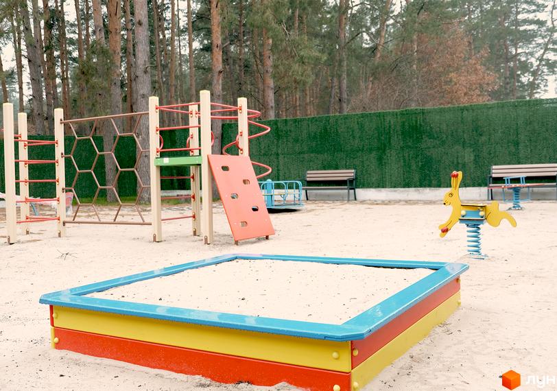 Дитячий майданчик у Таунхауси Green Heaven з пісочницею, гіркою та гойдалкою. Навколо зелена огорожа та дерева.