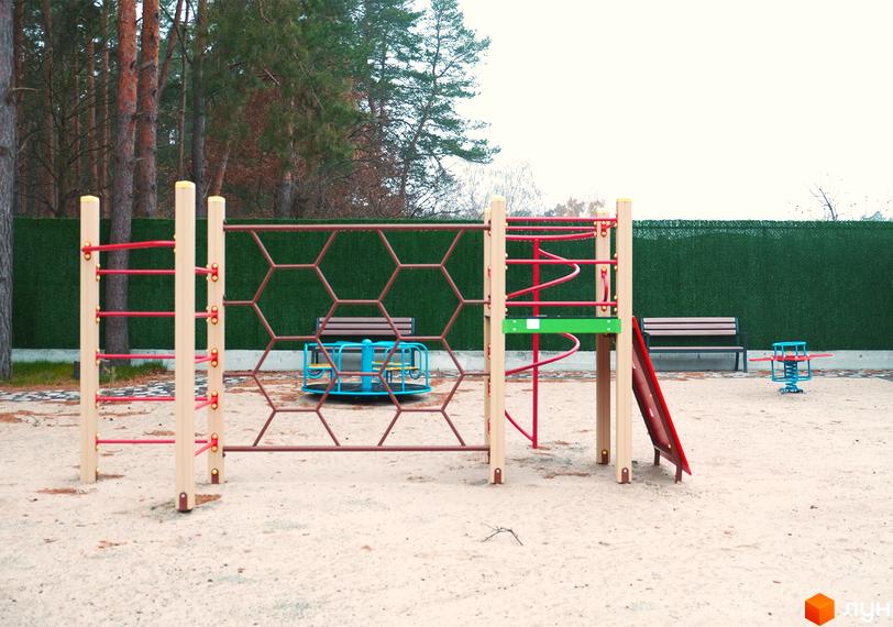 Дитячий майданчик з гіркою, каруселлю та гойдалкою на піщаному покритті біля житлового комплексу Green Heaven. На задньому плані зелений паркан та дерева.