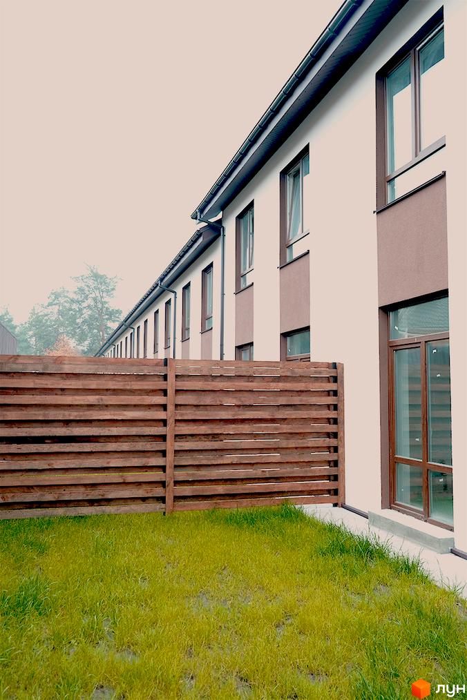 Фасад Таунхаусів Green Heaven з бежевими стінами та коричневими вікнами. Перед будинками розташований дерев'яний паркан та зелений газон.