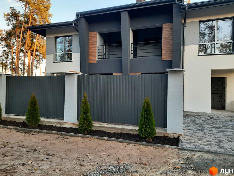 Фасад таунхаусів Rest Home з сірим парканом та зеленими туями. Прибудинкова територія з бруківкою та піском.