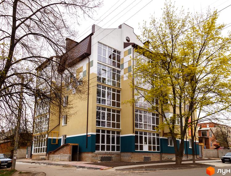 Зовнішній вигляд новобудови на вулиці Коржівська, 54, з великою кількістю вікон та елементами дизайну. Навколо будинку видно дерева та прибудинкову територію.