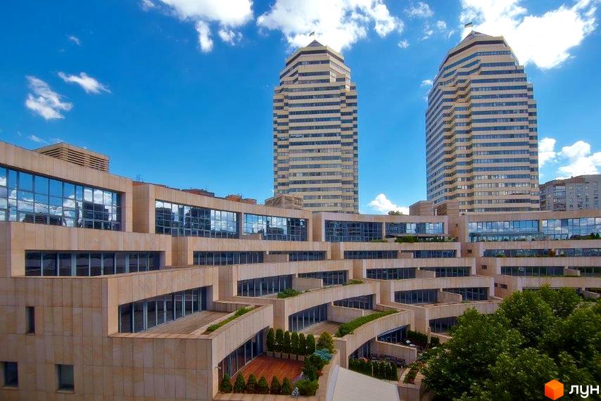 Житловий комплекс Амфітеатр з двома висотними будинками та сучасною прибудинковою територією, озелененою рослинами.