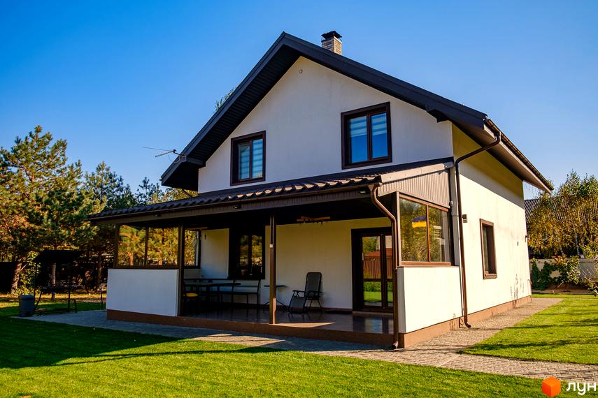 Котеджне містечко Калина-2: двоповерховий будинок з терасою та доглянутим газоном. Навколо будинку зелені насадження та сонячне небо.