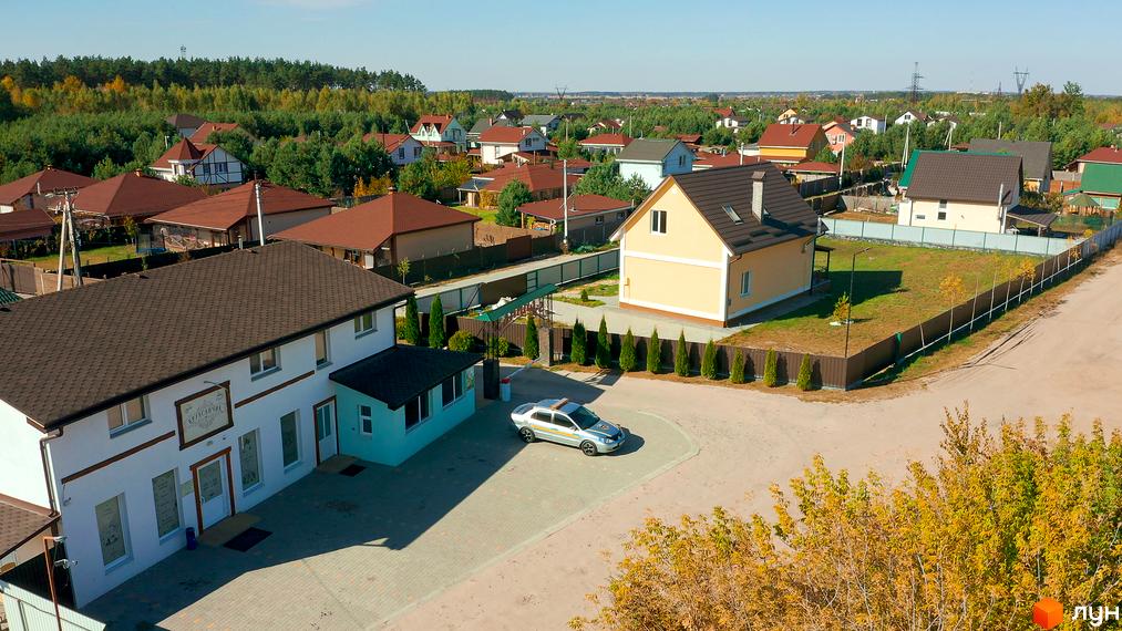 Котеджне містечко Калина-2: двоповерхові будинки з коричневими дахами та зеленою прибудинковою територією. На території комплексу є парковка та доглянуті дерева.