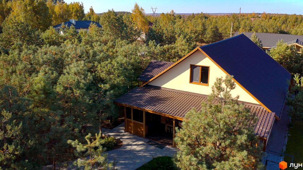 Котеджне містечко Калина-2: двоповерховий будинок з коричневим дахом серед зелених дерев. Прибудинкова територія з доріжками та зеленню.