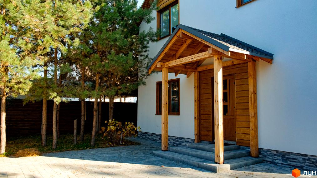 Котеджне містечко Калина-2: вхідна група з дерев'яним навісом та дверима, поруч зелені дерева та вимощена доріжка.