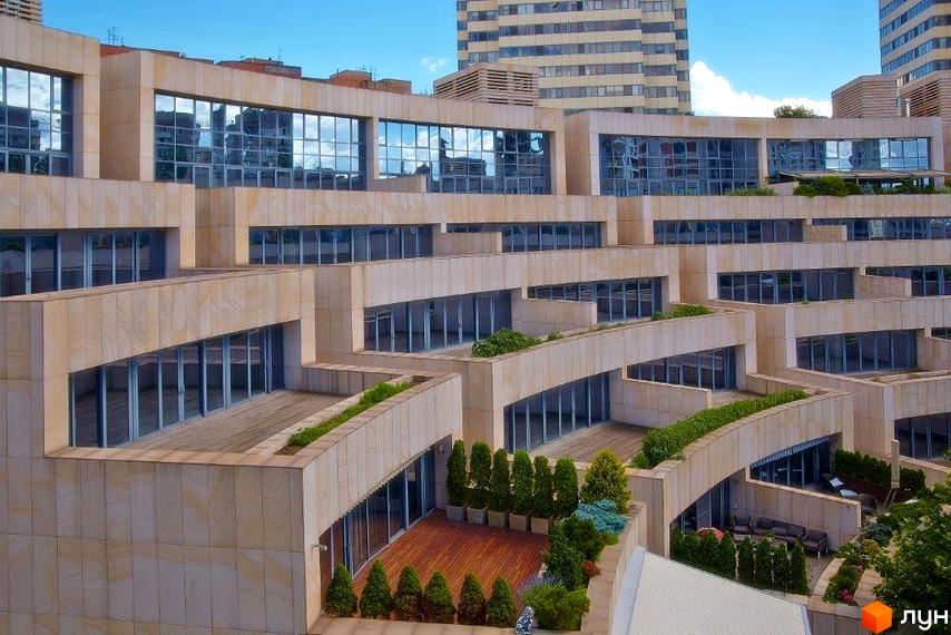 Зовнішній вигляд житлового комплексу Амфітеатр з великими вікнами та терасами. Прибудинкова територія озеленена та облаштована для відпочинку.