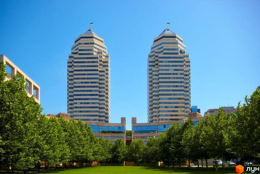 Житловий комплекс Амфітеатр з двома висотними будинками на фоні зелених дерев та чистого неба.