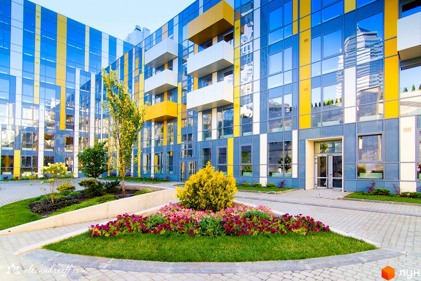 Зовнішній вигляд житлового комплексу ЖК Фестивальний з яскравими фасадами. Прибудинкова територія з зеленими насадженнями та квітниками.