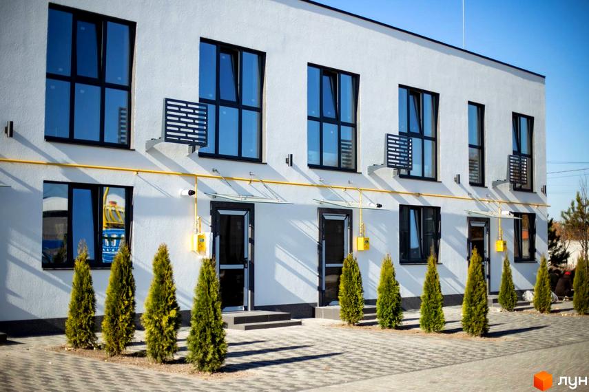 Таунхауси DREAM HOUSE з білими фасадами, чорними вікнами та індивідуальними входами. Перед будинками висаджені туї та облаштований бруківкою двір.