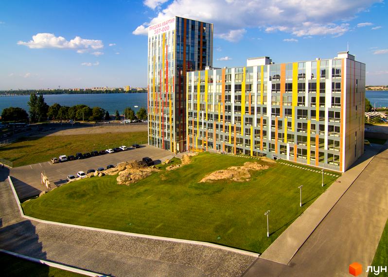 Житловий комплекс ЖК Фестивальний з кольоровими фасадами та прибудинковою територією з газоном і парковкою.