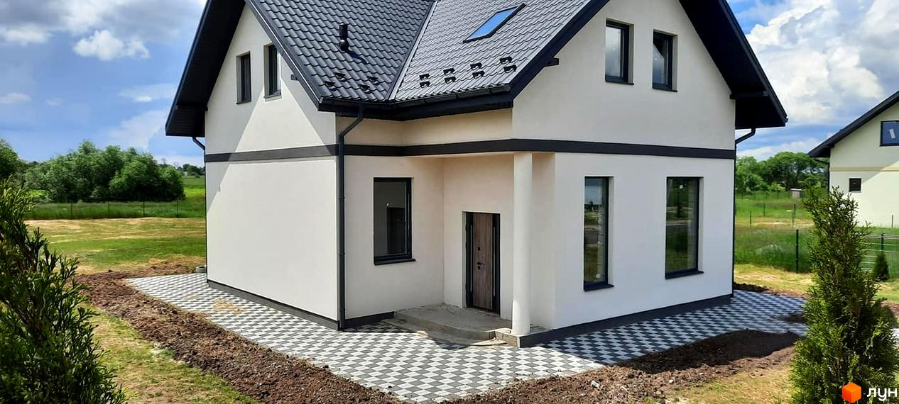 Білосніжний будинок з чорним дахом та вікнами. Перед будинком викладена плитка, поруч зелені насадження, що створюють затишну атмосферу.