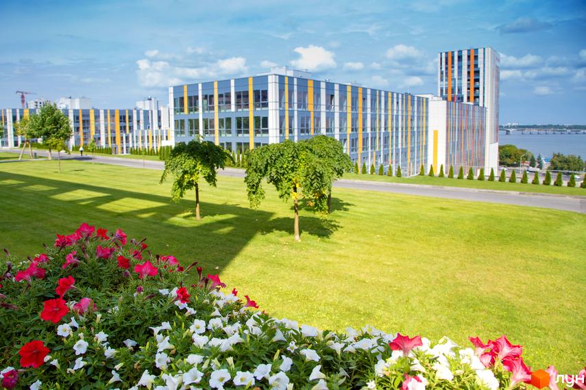 Будівлі Житлового комплексу Фестивальний з фасадами сірих, білих та помаранчевих панелей. Перед ними зелений газон з деревами та квітковими клумбами.