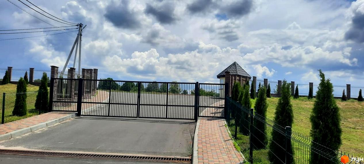 Котеджне містечко КМ Лелека: в'їзд на територію через металеві ворота з кам'яними колонами, огороджена територія з туями та парканом.