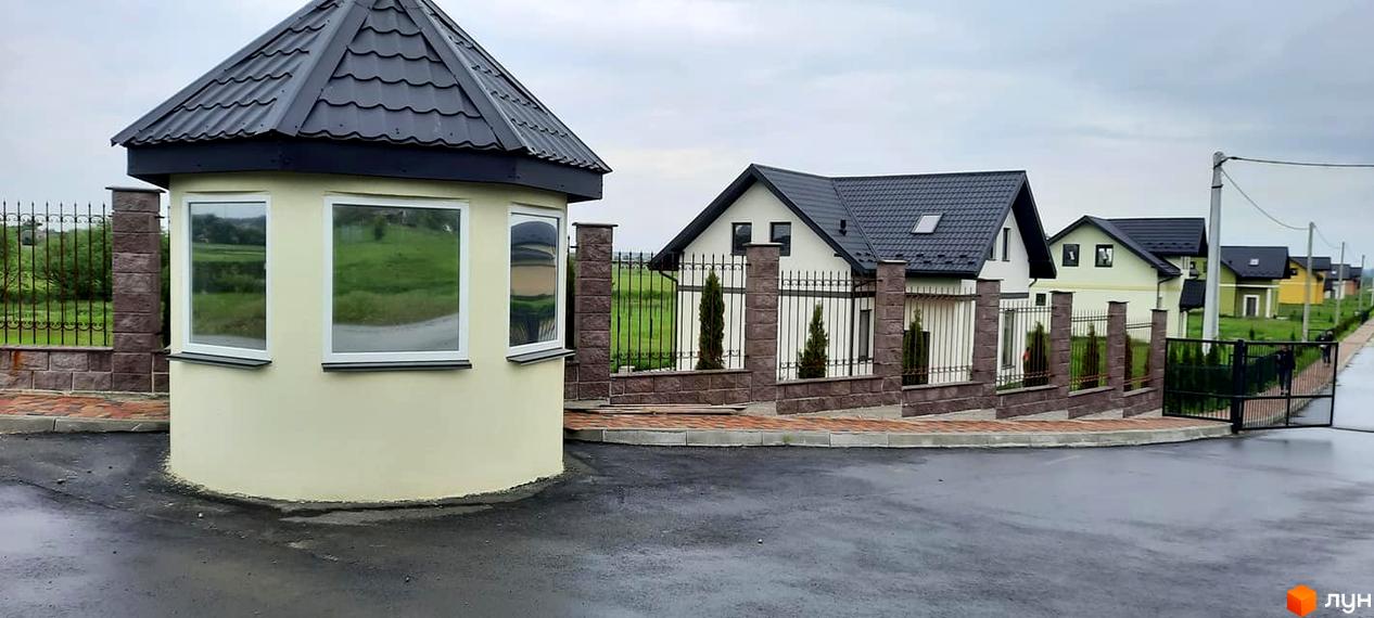 Охоронна будівля з вікнами та козирком, поруч з будинками та огорожею. Містечко котеджів Лелека - ідеальне місце для вашого життя.